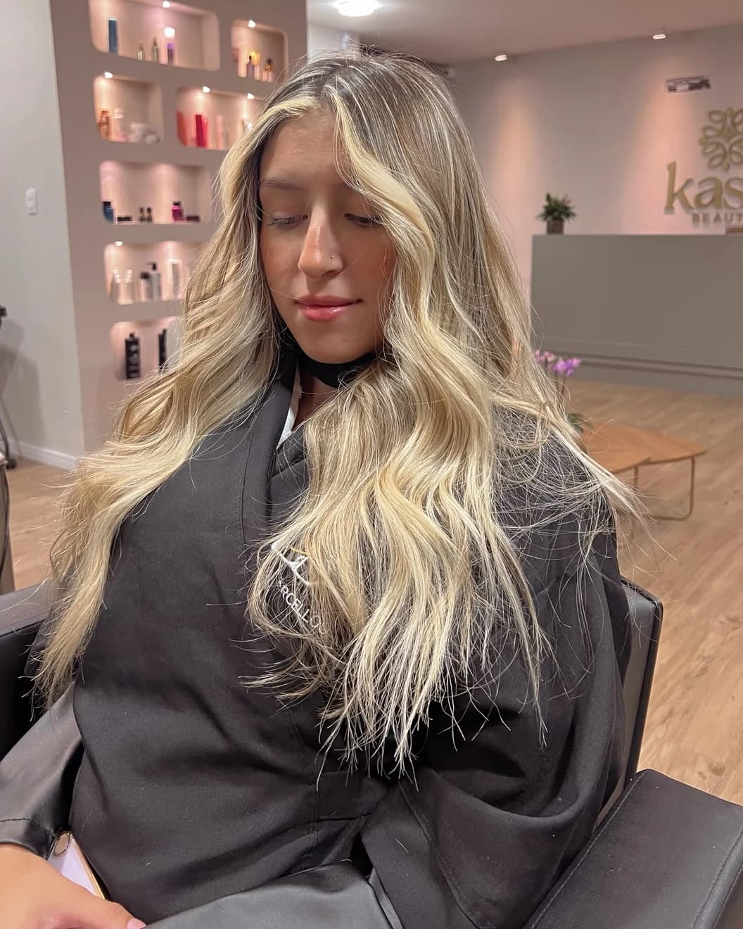 Cliente com balayage loiro na recepção da Kasa Beauty, com a placa da marca ao fundo
