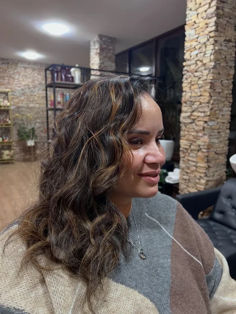 Cliente sorrindo com luzes acobreadas em cabelo cacheado, feitas no salão da Kasa Beauty