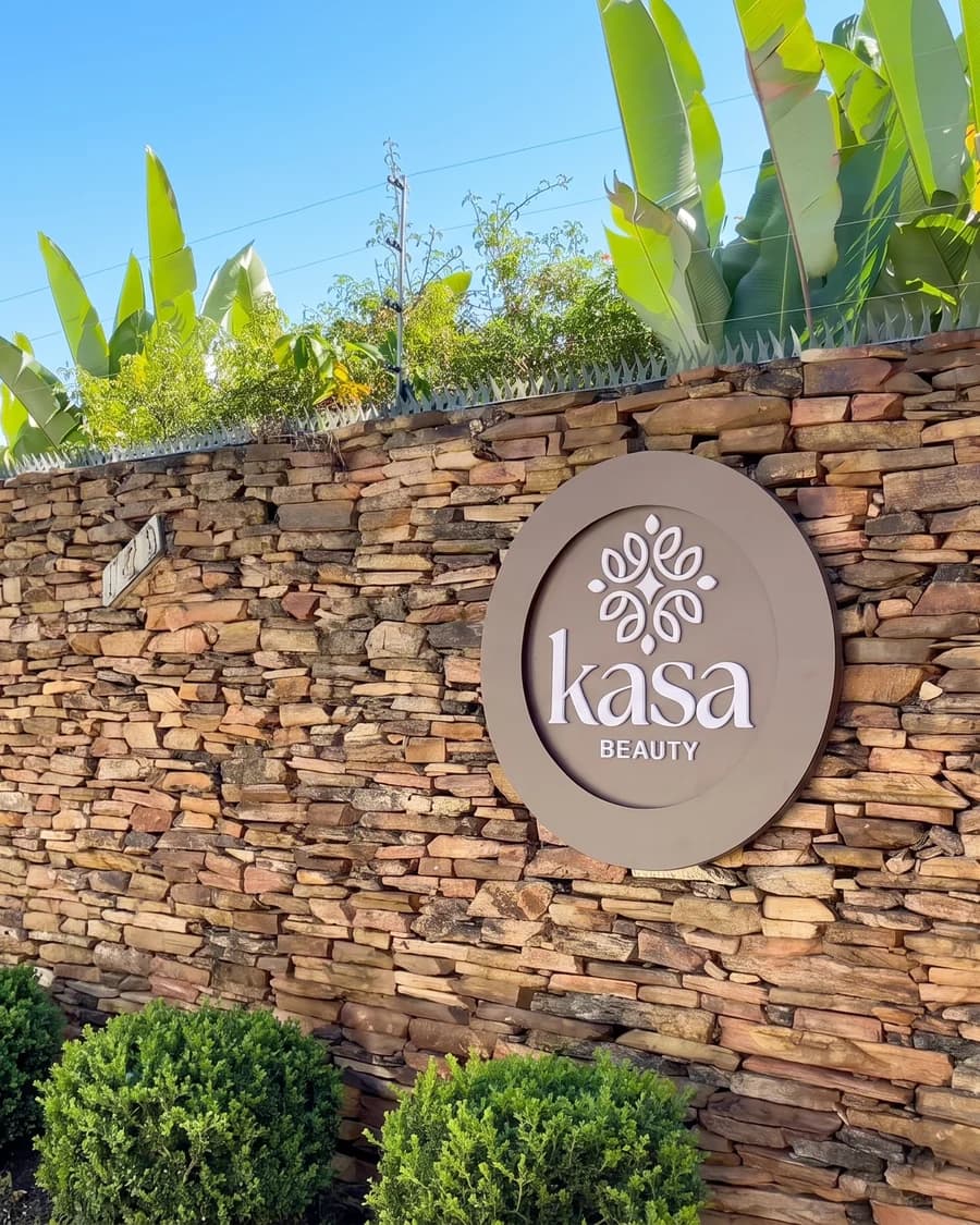 Fachada da Kasa Beauty: placa redonda com o logo na parede de pedra, na Rua Professor Carlos Pereira da Silva